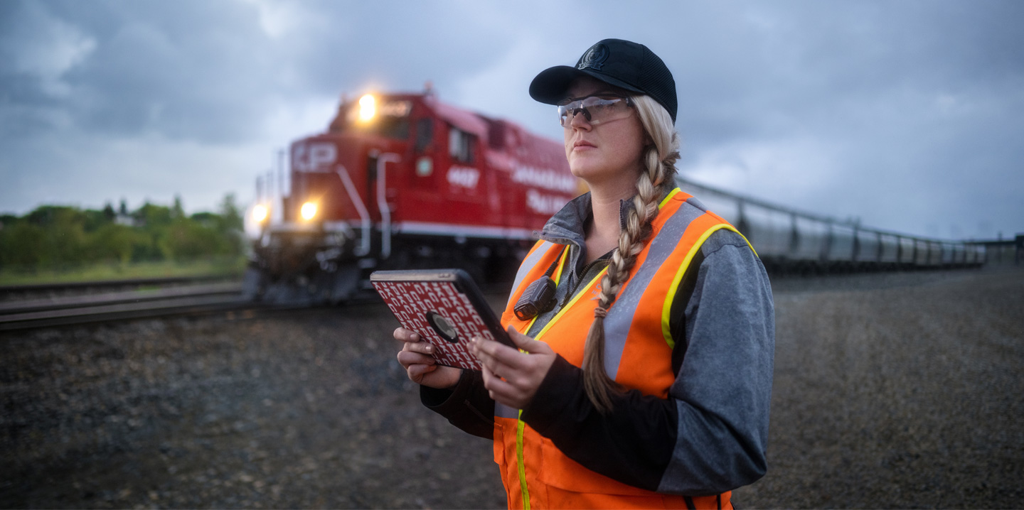 Een spoorwegmedewerker houdt een iPad vast en kijkt uit over het spoor terwijl er een trein voorbij rijdt